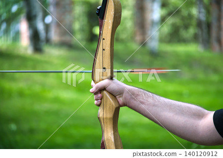 Archers hand gripping a wooden bow, arrow in flight against a blurred green background Archers hand gripping a wooden bow, arrow in flight against a blurred green background 140120912