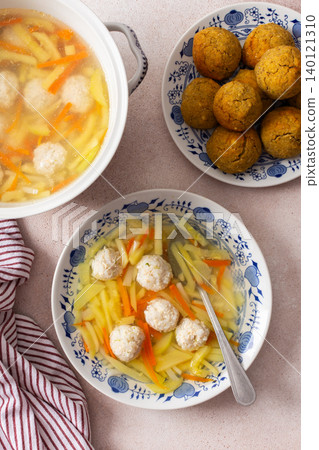 A bowl of vegetable soup with chicken meatballs is served alongside chickpea buns on a table. Fresh ingredients create a hearty meal for breakfast or lunch 140121310