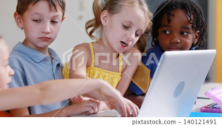 Pointing blonde girl in yellow dress reading at school table, with silver laptop, pink pencil case Pointing blonde girl in yellow dress reading at school table, with silver laptop, pink pencil case 140121491