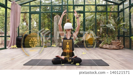 Meditating woman in sportswear using VR headset on mat in greenhouse with AR overlay and smartwatch Meditating woman in sportswear using VR headset on mat in greenhouse with AR overlay and smartwatch 140121571