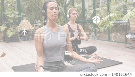 Meditating woman wearing headset, watch, sitting on mat in glass studio with plants, AR ship icons Meditating woman wearing headset, watch, sitting on mat in glass studio with plants, AR ship icons 140121644