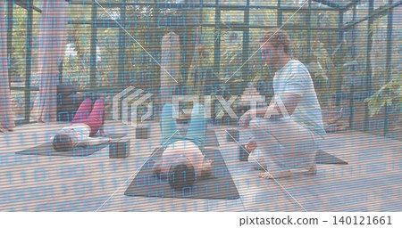 Guiding coach kneeling beside central student in teal leggings correcting posture on mats in studio Guiding coach kneeling beside central student in teal leggings correcting posture on mats in studio 140121661