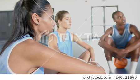 Sitting foreground woman in light blue jersey, resting on knees at gym court, orange basketball Sitting foreground woman in light blue jersey, resting on knees at gym court, orange basketball 140121669