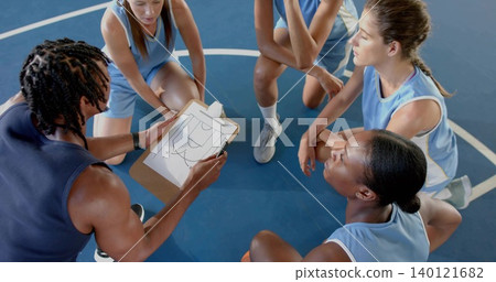Pointing braided coach holding clipboard on blue court players in blue jerseys listening near ball 140121682