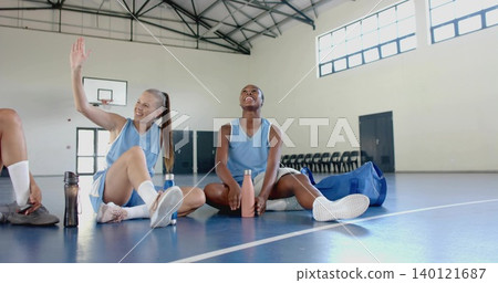 Sitting two female players wearing light blue uniforms chatting on gym court, holding water bottles Sitting two female players wearing light blue uniforms chatting on gym court, holding water bottles 140121687