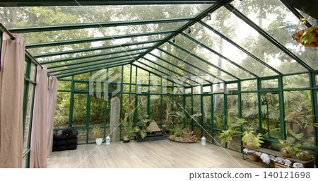 Displaying green metal-framed conservatory, showing pitched glass roof, potted plants, cushions 140121698