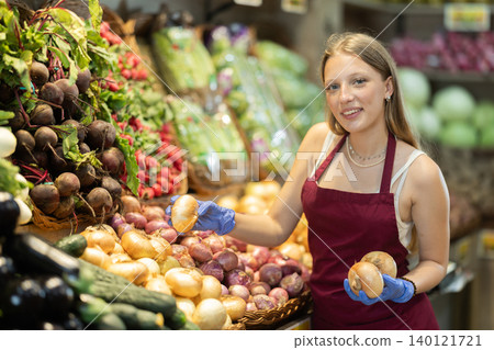 Girl shop seller add onion goods on display case in vegetable store Girl shop seller add onion goods on display case in vegetable store 140121721