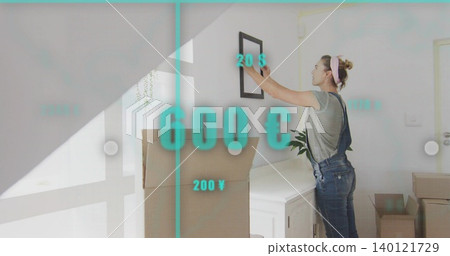 Hanging woman in overalls placing framed picture above white cabinet with AR overlays boxes plant Hanging woman in overalls placing framed picture above white cabinet with AR overlays boxes plant 140121729