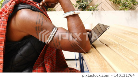 Leaning man tattooed arms with bracelets wearing plaid at wooden table in patio, with tablet cup Leaning man tattooed arms with bracelets wearing plaid at wooden table in patio, with tablet cup 140121764