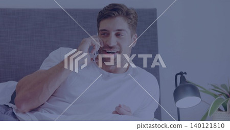 Smiling mid-adult man reclining on bed in bedroom, holding smartphone and wearing white T-shirt Smiling mid-adult man reclining on bed in bedroom, holding smartphone and wearing white T-shirt 140121810