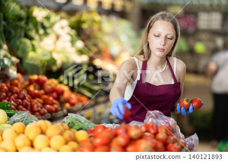 Girl shop seller add tomato goods on display case in vegetable store Girl shop seller add tomato goods on display case in vegetable store 140121893