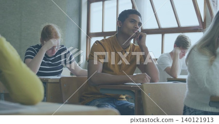 Leaning central student wearing mustard polo studying at high school desk, with papers pens Leaning central student wearing mustard polo studying at high school desk, with papers pens 140121913