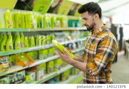 Adult man chooses liquid fertilizer for his garden at gardening supermarket Adult man chooses liquid fertilizer for his garden at gardening supermarket 140121976