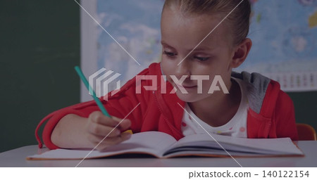 Writing student in red hoodie at school desk with open notebook, green pencil, chalkboard and map Writing student in red hoodie at school desk with open notebook, green pencil, chalkboard and map 140122154