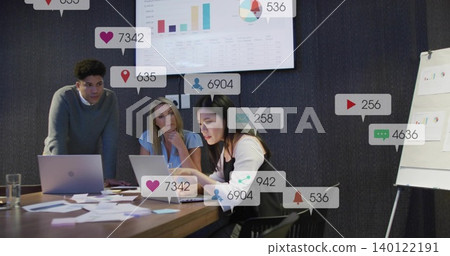 Reviewing team in office wear studying charts in boardroom with wall display, laptops, social icons 140122191