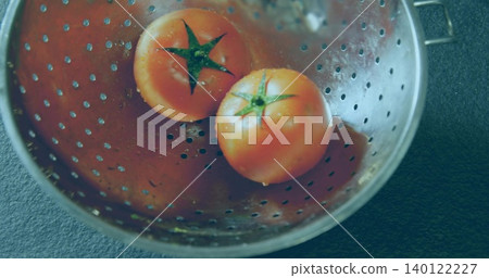 Showing perforated steel colander holding two ripe red tomatoes on kitchen countertop with droplets Showing perforated steel colander holding two ripe red tomatoes on kitchen countertop with droplets 140122227