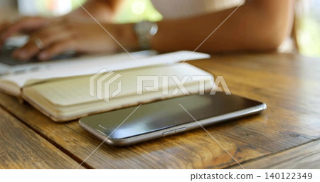 Lying smartphone at right front on wooden table at home, with notebook laptop watch sleeveless top Lying smartphone at right front on wooden table at home, with notebook laptop watch sleeveless top 140122349