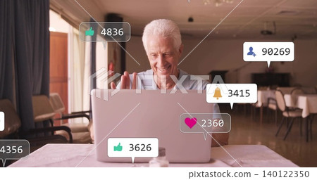 Waving senior man in light-blue polo using silver laptop in dining area, notifications, salt shaker Waving senior man in light-blue polo using silver laptop in dining area, notifications, salt shaker 140122350