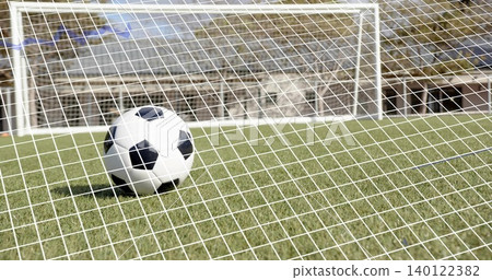 Resting classic black-and-white soccer ball sitting on trimmed grass at stadium, goal net visible 140122382