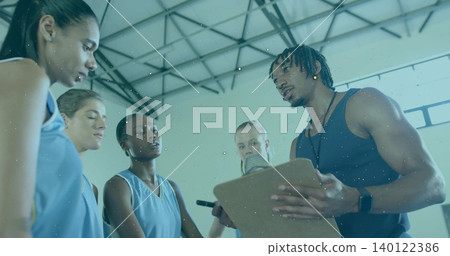 Talking coach in dark tank holding clipboard at gym with players in light-blue jerseys, copy space Talking coach in dark tank holding clipboard at gym with players in light-blue jerseys, copy space 140122386