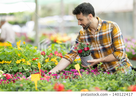 Man customer inspect shelves filled with flowers, hold pot with garden carnation plant 140122417
