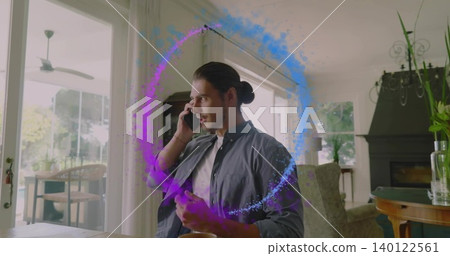 Talking bun-haired man in dark shirt holding phone, gesturing at wooden table at home, purple ring Talking bun-haired man in dark shirt holding phone, gesturing at wooden table at home, purple ring 140122561