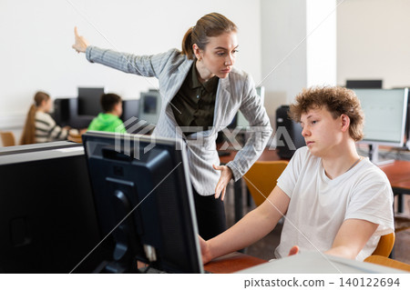 Strict teacher reprimanding negligent teenage student in computer class Strict teacher reprimanding negligent teenage student in computer class 140122694