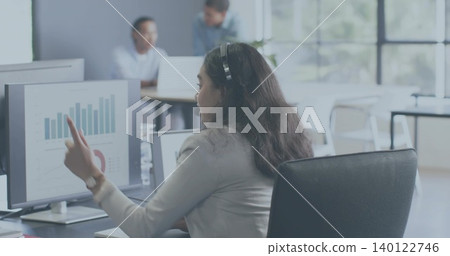 Pointing woman in light blazer wearing headset presenting data on monitor in open office Pointing woman in light blazer wearing headset presenting data on monitor in open office 140122746