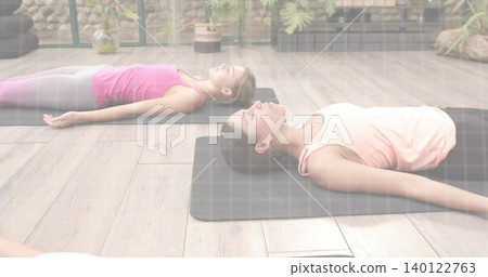 Lying adult women practicing relaxation pose in yoga studio on black mats, wearing tank tops Lying adult women practicing relaxation pose in yoga studio on black mats, wearing tank tops 140122763