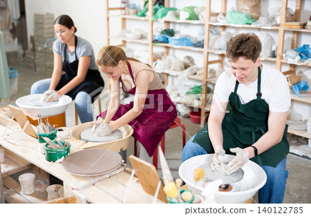 Young woman teacher and two teenagers make products on potter's wheel Young woman teacher and two teenagers make products on potter's wheel 140122785