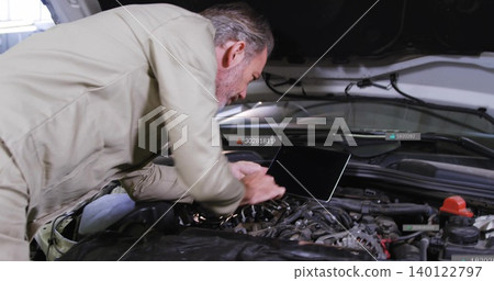Leaning senior man in tan jacket inspecting engine in garage, with laptop, battery and fender cover Leaning senior man in tan jacket inspecting engine in garage, with laptop, battery and fender cover 140122797