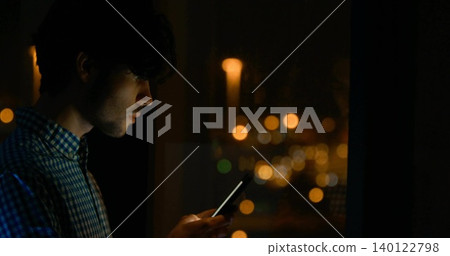 Holding adult male staring at smartphone screen in dim room by window, checked shirt, copy space Holding adult male staring at smartphone screen in dim room by window, checked shirt, copy space 140122798