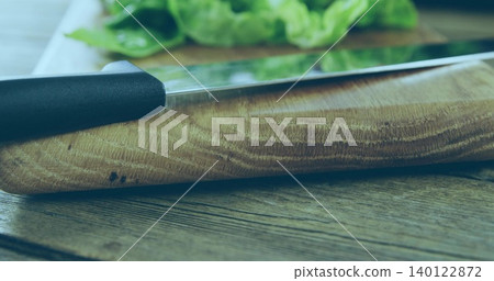 Showing wooden cutting board grain on wooden tabletop, with metal knife black handle and greens Showing wooden cutting board grain on wooden tabletop, with metal knife black handle and greens 140122872