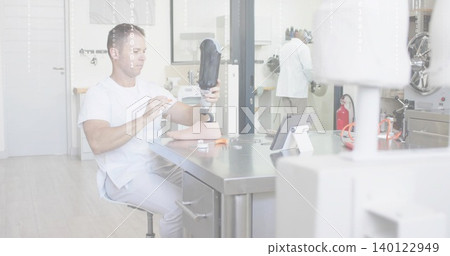 Inspecting seated clinician wearing white scrubs handling prosthetic socket and foot at workbench Inspecting seated clinician wearing white scrubs handling prosthetic socket and foot at workbench 140122949