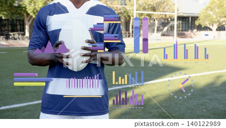 Holding white football, male athlete wearing navy blue and white jersey on turf with AR charts Holding white football, male athlete wearing navy blue and white jersey on turf with AR charts 140122989