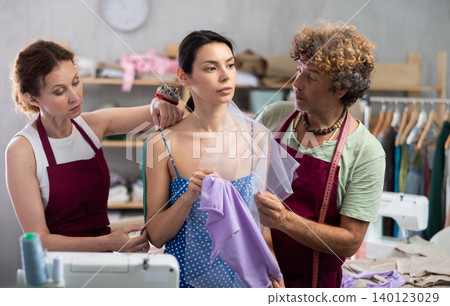 Female dressmaker and male tailor trying on fabric decoration on female dress and take measurements Female dressmaker and male tailor trying on fabric decoration on female dress and take measurements 140123029