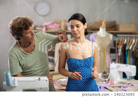 Middle-aged male tailor measuring female client in sewing workshop Middle-aged male tailor measuring female client in sewing workshop 140123093