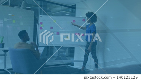 Pointing woman wearing blue top placing pink sticky note on board in office, man holding notebook Pointing woman wearing blue top placing pink sticky note on board in office, man holding notebook 140123129