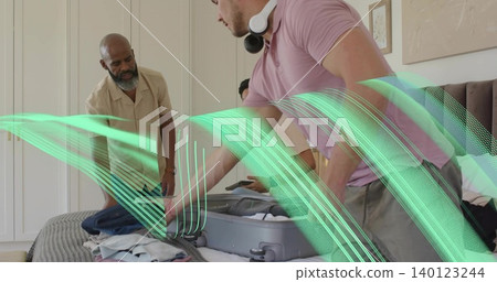 Packing man in pink polo leaning over suitcase in bedroom, with white headphones and tablet Packing man in pink polo leaning over suitcase in bedroom, with white headphones and tablet 140123244