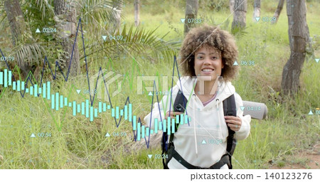 Smiling hiker wearing light hoodie holding backpack with roll mat on grassy trail with charts 140123276