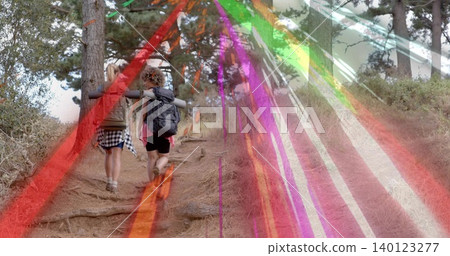 Hiking two women climbing pine path in shorts carrying backpacks and rolled pads with light streaks Hiking two women climbing pine path in shorts carrying backpacks and rolled pads with light streaks 140123277