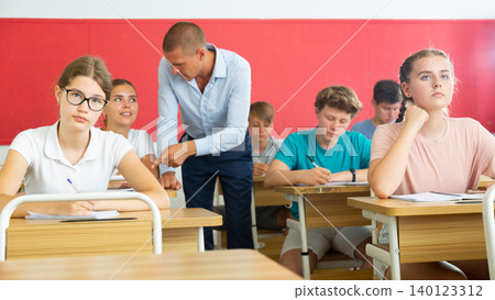 Focused teenage students studying in classroom with teacher, writing lectures in workbooks 140123312