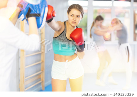 Girls works out strength and speed of boxing punch mitts with help of partner in boxing paws Girls works out strength and speed of boxing punch mitts with help of partner in boxing paws 140123329