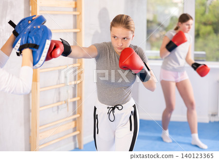 Girl teenager with her trainer in gym learns to hit punch mitts 140123365