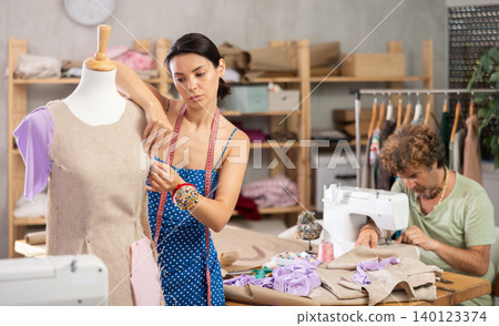 Middle-aged male dressmaker sewing while woman working with mannequin 140123374