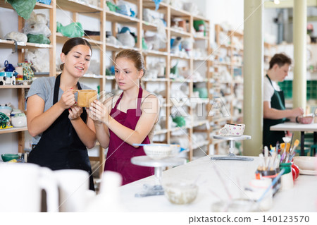 Young woman examines ceramic cup made by teenage girl Young woman examines ceramic cup made by teenage girl 140123570