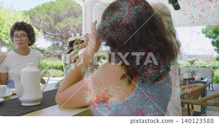 Sitting woman wearing sleeveless blue top chatting on shaded patio with teapot, flower crown 140123588
