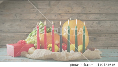 Displaying kinara seven lit candles glowing on worn pale-blue tabletop with pumpkin grapes red gift Displaying kinara seven lit candles glowing on worn pale-blue tabletop with pumpkin grapes red gift 140123646