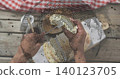 Handling mid adult male hands with bare forearms pulling round flatbreads on wooden deck, with fork 140123705