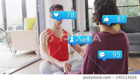 Sitting partners holding hands cross-legged at home in red top and maroon top with blue bubbles Sitting partners holding hands cross-legged at home in red top and maroon top with blue bubbles 140123826